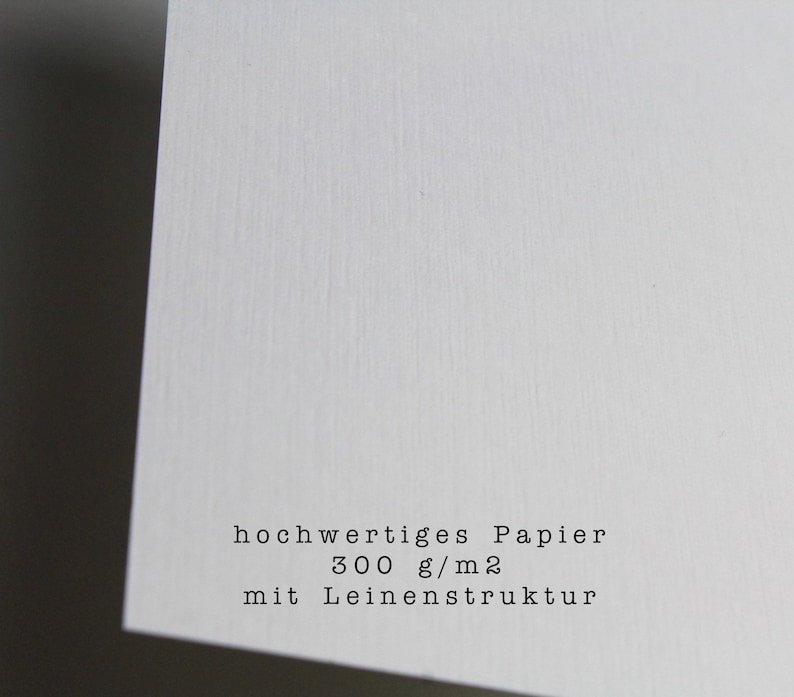 May include: Close-up of a white textured paper with the text "hochwertiges Papier 300 g/m2 mit Leinenstruktur".