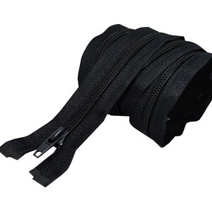 May include: A black zipper with a metal slider. The zipper is coiled and ready to be sewn into a garment or project.