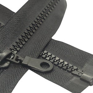 May include: Black zipper with a black plastic slider and pull tab. The zipper is closed and the teeth are visible.