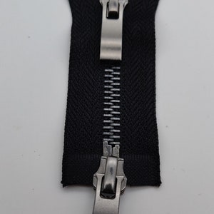 May include: A black zipper with a silver metal slider. The zipper is closed and the slider is in the middle of the zipper.
