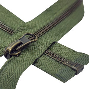 K&ouml;nnte beinhalten: Nahaufnahme eines gr&uuml;nen Rei&szlig;verschlusses mit einem Messing-Schieber und -Zipper. Der Rei&szlig;verschluss ist ge&ouml;ffnet und die Z&auml;hne sind sichtbar.