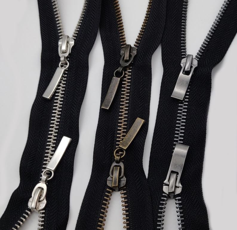 May include: Three black zipper tapes with different colored metal zipper pulls. The zipper pulls are silver, gold, and bronze.
