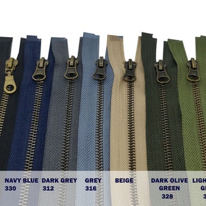 May include: A close-up of ten zipper pulls in various colours, including black, navy blue, dark grey, grey, beige, dark olive green, and light olive green. The zipper pulls have a brass finish.