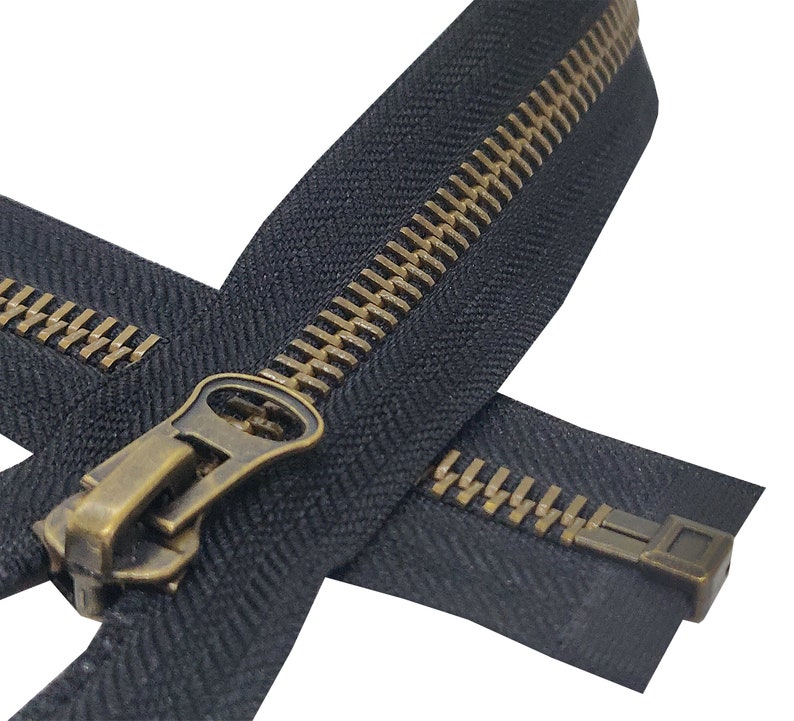 K&ouml;nnte beinhalten: Ein schwarzer Rei&szlig;verschluss mit einem Messing-Schieber und -Zipper. Der Rei&szlig;verschluss ist geschlossen und die Z&auml;hne sind sichtbar.