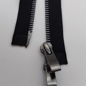May include: A black zipper with a silver slider. The zipper is open and the slider is in the middle of the zipper.