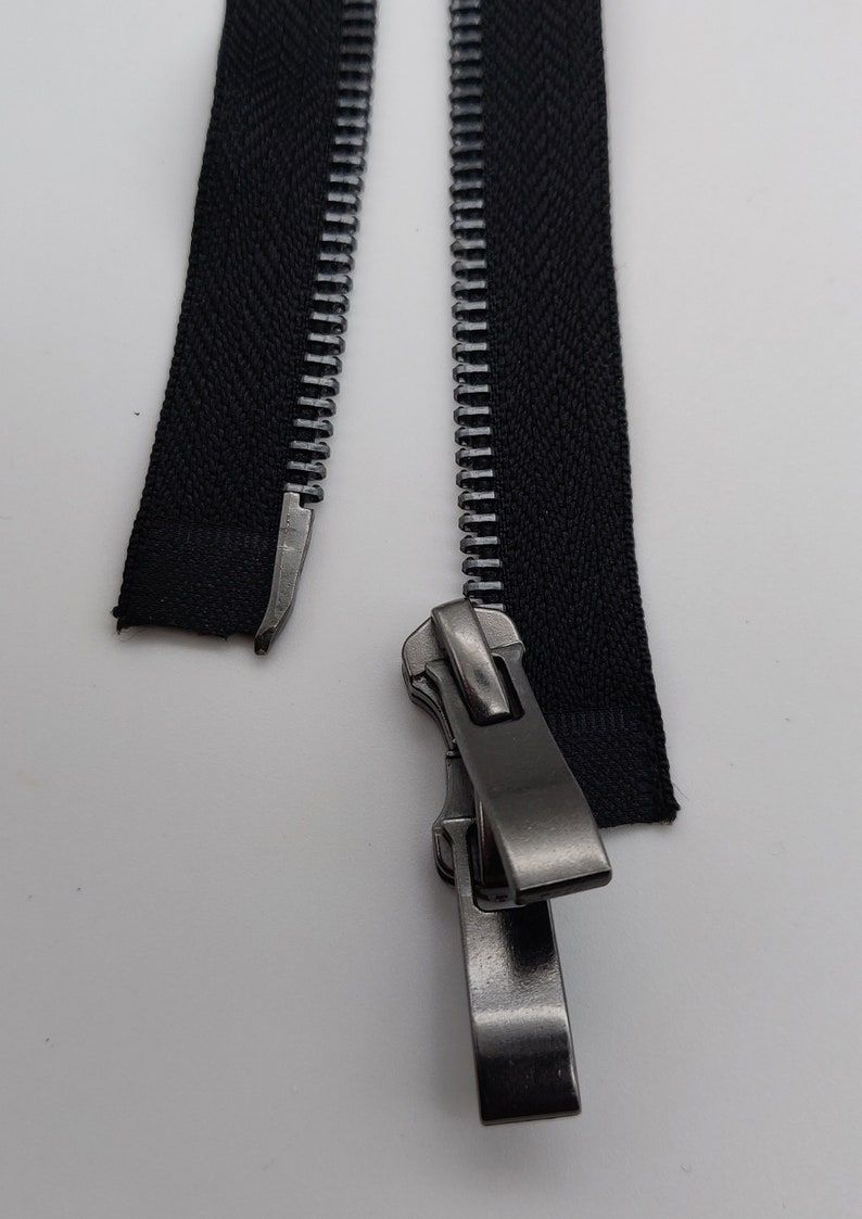 May include: A black zipper with a silver slider. The zipper is open and the slider is in the middle of the zipper.