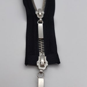 May include: A black zipper with a silver slider and pull tab. The zipper is open and the slider is in the middle of the zipper.