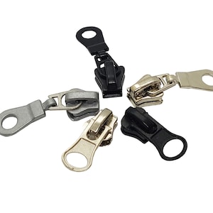 May include: Four zipper pulls in different colours: black, silver, gold, and a combination of silver and gold. Each pull has a circular loop at the end.