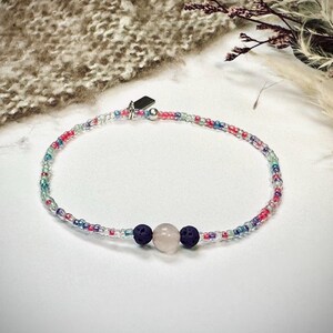 Könnte beinhalten: Ein zartes Perlenarmband mit einem rosa-weißen Steinanhänger und zwei dunkelblauen Lavasteinen.