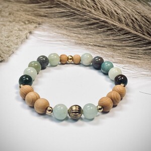 Könnte beinhalten: Ein grünes und braunes Perlenarmband mit einer goldenen Akzentperle. Das Armband ist aus Natursteinen und Holz gefertigt.