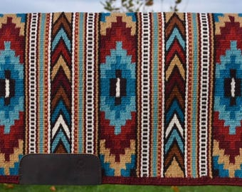 May include: A colorful saddle blanket with a geometric pattern in shades of red, blue, brown, and white. The blanket has a leather cinch strap.