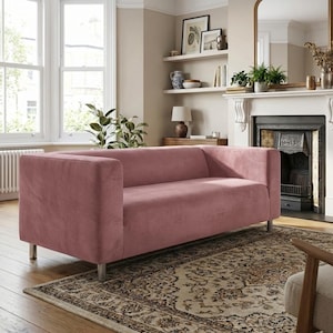 May include: A blush pink, contemporary sofa with a streamlined design. The sofa features a low back, square arms, and silver metal legs. It is situated in a living room with a patterned rug and a fireplace.