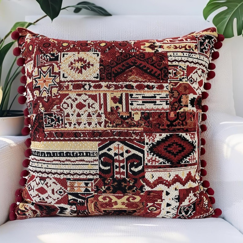 Burgundy patchwork cushion cover with pom pom trim on a white sofa