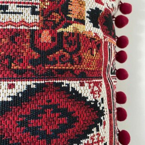 Pom pom cushion close-up: trim and woven burgundy pattern