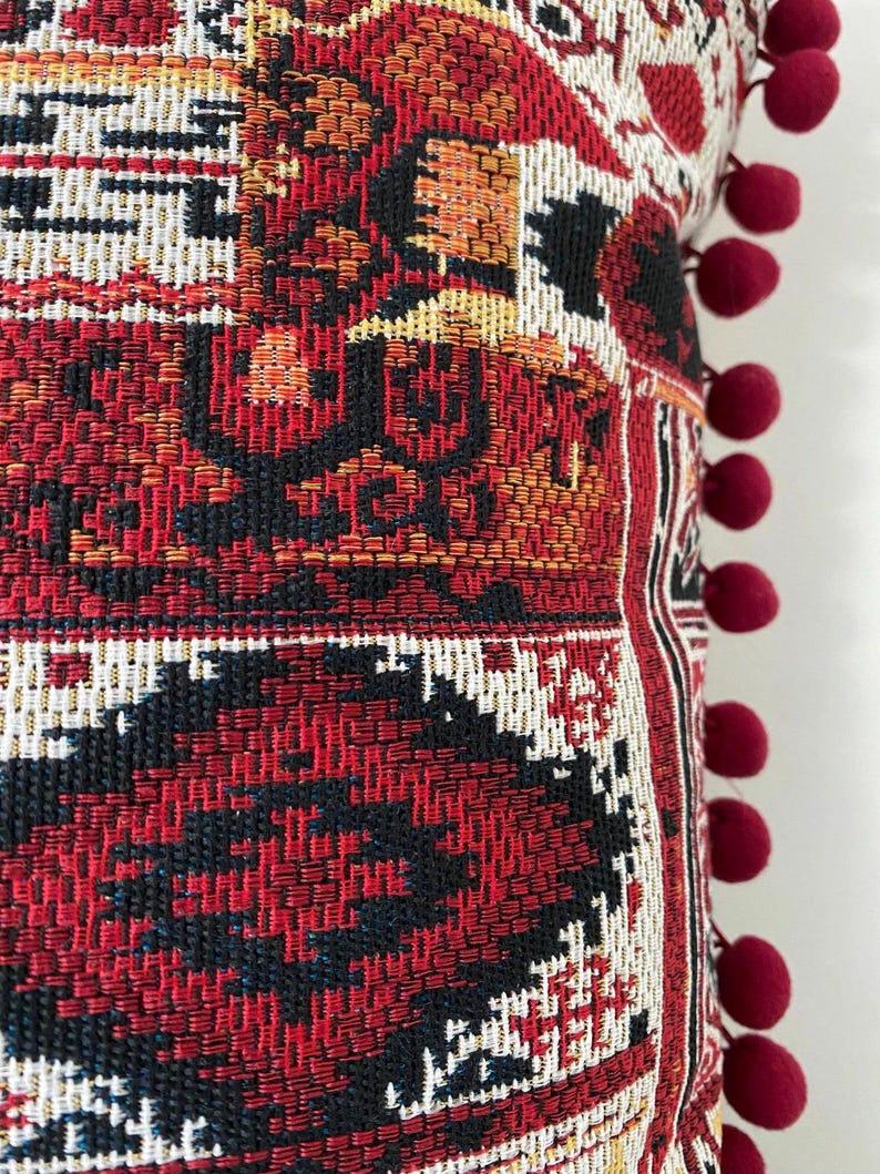 Pom pom cushion close-up: trim and woven burgundy pattern