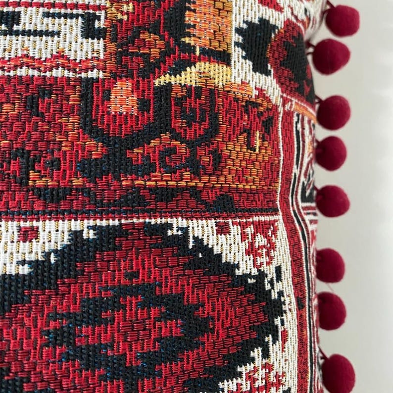 Kilim cushion close-up: woven patchwork and burgundy pom poms