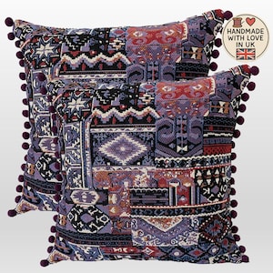 May include: Two square cushions with a patchwork design in shades of purple, red, black, and white. Each cushion has a border of small, dark purple pom-poms. The cushions are labelled "Handmade with Love in UK".