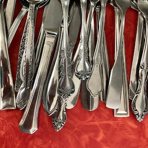 May include: A collection of silver cutlery, including forks, spoons, and knives, arranged in a fan shape on a red background.