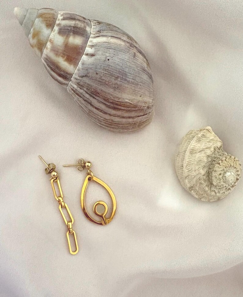 May include: A pair of mismatched gold-toned earrings. One earring features a vertical chain of three rectangular links, while the other earring consists of a teardrop-shaped frame with a small circular cutout in the center. Both have stud backings.