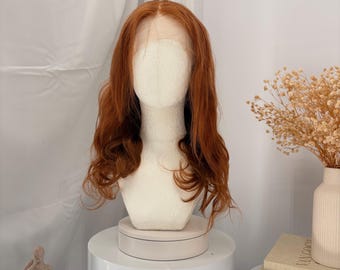 May include: A long, wavy, copper-red wig displayed on a white mannequin head. The wig features a center part with a visible lace front, showcasing natural-looking hair texture and vibrant auburn tones that fall past the shoulders.