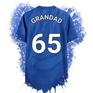 May include: A blue short-sleeved t-shirt featuring the word GRANDAD and the number 65 in white lettering on the back. The shirt has a subtle tonal pattern and is surrounded by a blue paint splatter effect that drips from the bottom hem.