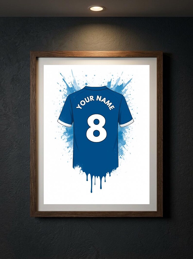May include: A framed print featuring a blue sports jersey with white trim, the number 8, and the text YOUR NAME. The design includes a blue watercolor splash effect behind the jersey and a blue paint drip effect at the bottom hem of the shirt.