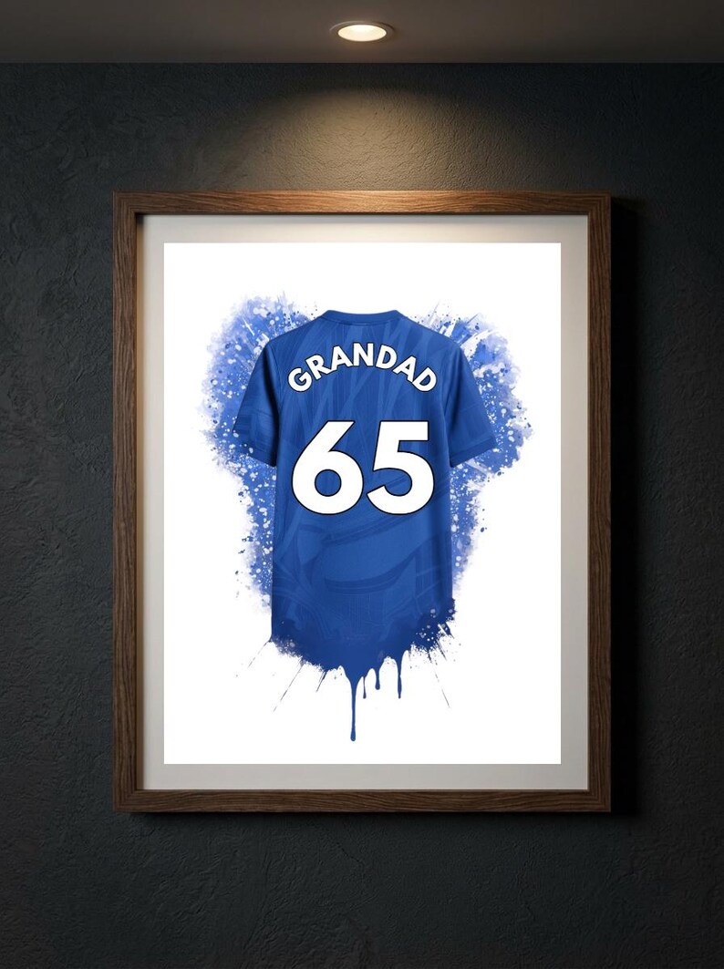 May include: A framed print featuring a blue sports jersey graphic with the word GRANDAD and the number 65 in white lettering. The design includes blue watercolor-style paint splatters and drips extending from the bottom of the jersey.