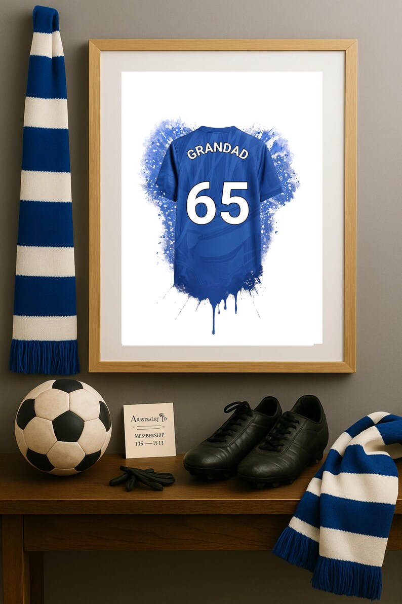 May include: A framed print featuring a blue sports jersey with the text GRANDAD and the number 65 in white. The jersey design includes a blue watercolor splash effect. The print is displayed alongside a soccer ball, black cleats, and blue and white scarves.