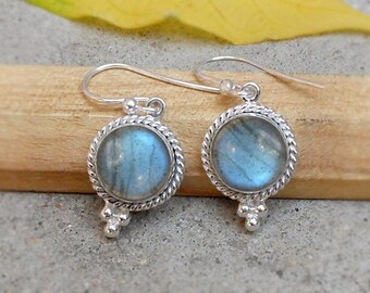 May include: A pair of silver earrings with round, blue-gray labradorite stones. The stones are set in a twisted rope-like border and have a small cluster of silver beads below. The earrings hang from simple silver hooks.