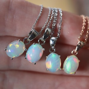 May include: Four necklaces with oval-shaped opal pendants. The pendants display a play of color, with flashes of blue, green, and pink. The chains are silver and rose gold, and the opals are held in place by small prongs.