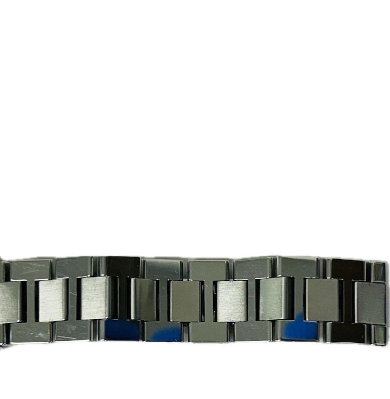 May include: Close-up of a silver metal watch band. The band is composed of rectangular links with a brushed finish. The links are connected to each other, forming a flexible chain. The watch band is against a white background.