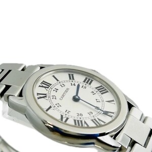 May include: A silver-toned wristwatch with a white face and black Roman numeral hour markers. The watch features a silver band and the brand name "CARTIER" is visible on the watch face. The watch hands point to the time.