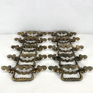 May include: A collection of antique brass drawer pulls. Each pull features an ornate design with a twisted handle and decorative end pieces. The pulls are arranged in rows, showcasing their intricate details and aged patina.