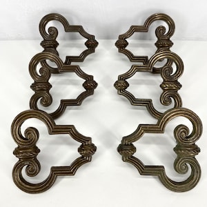 May include: Four antique bronze-colored drawer pulls. Each pull features an ornate design with scrolled ends and a central rectangular shape. The pulls are symmetrical and appear to be made of metal, likely brass or bronze.