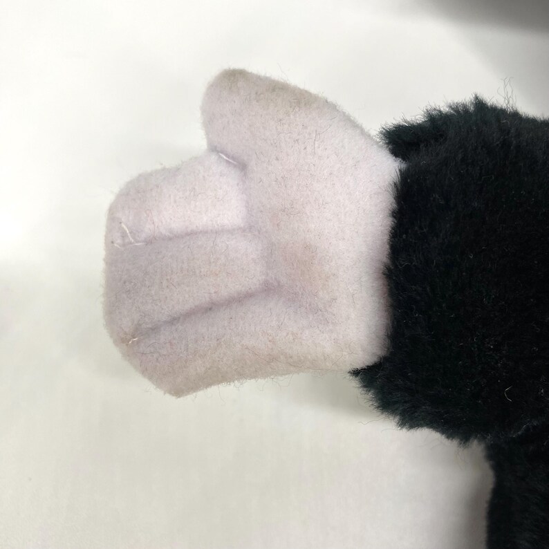May include: A plush toy hand giving a thumbs-up. The hand is light pink, with a black furry sleeve. The toy is made of soft fabric and is likely part of a larger stuffed animal.