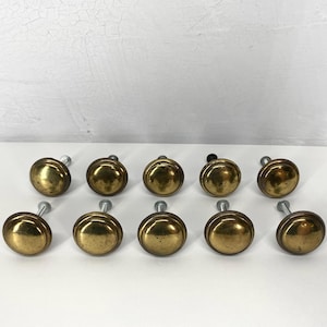 May include: A collection of ten antique brass cabinet knobs. Each knob has a rounded, domed shape with a brass finish and a silver-colored screw. The knobs are arranged in two rows of five against a white background.
