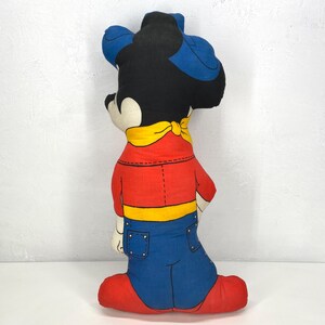 May include: A vintage Mickey Mouse plush doll, featuring a black head with blue ears and a red shirt with blue jeans. The doll has a yellow neckerchief and red shoes. The plush is a classic cartoon character collectible.