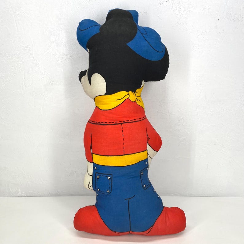 May include: A vintage Mickey Mouse plush doll, featuring a black head with blue ears and a red shirt with blue jeans. The doll has a yellow neckerchief and red shoes. The plush is a classic cartoon character collectible.