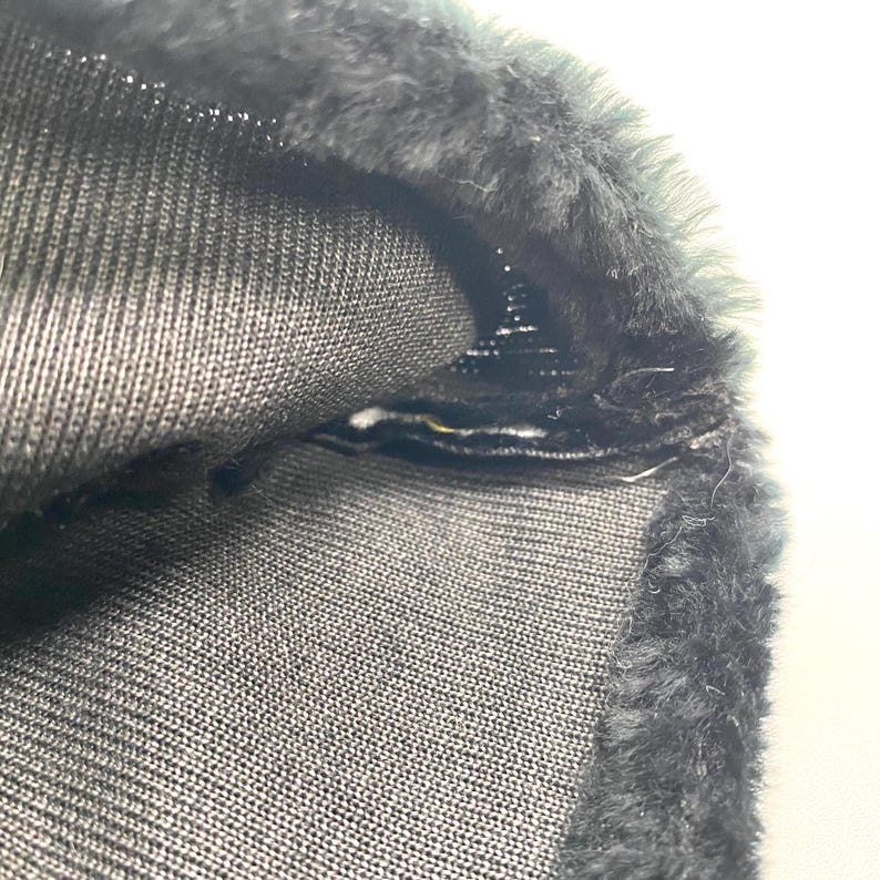 May include: Close-up of a section of dark grey fabric with a textured knit pattern. The edge is trimmed with a band of dark grey faux fur. The fabric is folded over, revealing the interior construction and stitching.