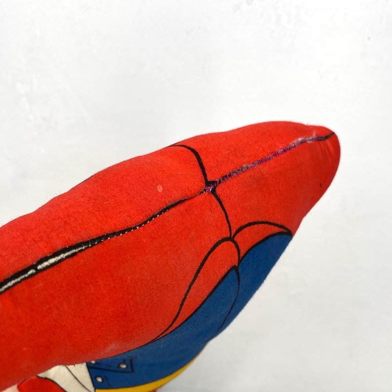 May include: A red and blue plush toy with black outlines. The toy has a red body with black lines and blue accents. The toy is made of a soft material and is likely a children's toy.
