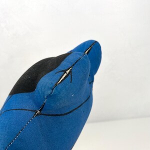 May include: A blue and black fabric object with a stitched seam. The object has a curved shape with a black section and a blue section with black lines and white accents. The background is white.