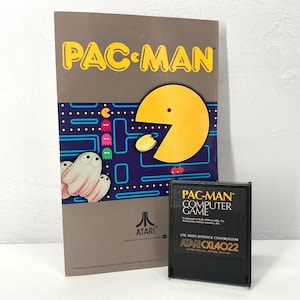 May include: A vintage Pac-Man computer game cartridge and box. The box features the Pac-Man logo in yellow, along with the iconic Pac-Man character and ghosts. The cartridge is black with yellow text.