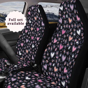 Può includere: Un paio di coprisedili per auto neri con un motivo a cuore rosa e bianco e un'impronta di leopardo. Il testo "Full set available" è visibile nell'immagine.