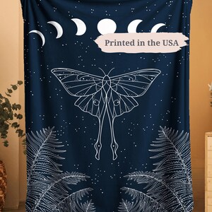 May include: A navy blue blanket with a white moth design, moon phases, and fern patterns. The blanket has a starry night sky design and the text "Printed in the USA".