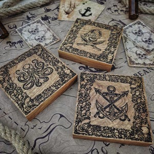 Könnte beinhalten: Holzkisten mit Piratenmotiven, darunter ein Oktopus, Totenkopf und gekreuzte Knochen sowie ein Anker. Die Kisten sind quadratisch mit aufwendigen Bordüren. Spielkarten mit nautischen Symbolen sind ebenfalls vorhanden.