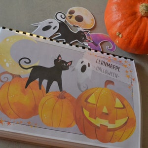 May include: A Halloween learning book with a black cat, a ghost, and pumpkins. The book cover features the text "Lernmappe - HALLOWEEN -" and a crescent moon.