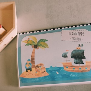 以下が含まれることがあります： 黒いドクロと交差した骨の旗を掲げた海賊船、ヤシの木、宝箱を持った海賊が描かれた、子供向けのカラフルな学習マップ。マップのタイトルは「LERNMAPPE - PIRATEN - 」です。