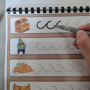 May include: A workbook with dotted lines for tracing the letter "c" and wavy lines. The page features illustrations of a treasure chest, a pirate, and a pile of gold coins.