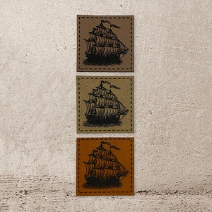 Könnte beinhalten: Drei Leder-Patches mit einem gestickten Rand, jeder mit einer Schwarzweiß-Illustration eines Segelschiffs mit vollen Segeln.