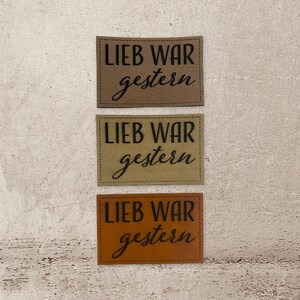 Könnte beinhalten: Drei braune Lederpatches mit dem Text "Lieb war gestern" in schwarzer Schrift.